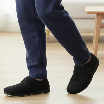 Black microsuede men's slippers on feet, slip-on with padded strap detail.