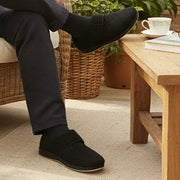 Black microsuede slippers on feet, side angle showing low sole and strap.