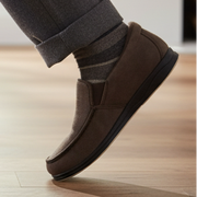 Men's brown slip-on slippers with black sole worn with gray pants
