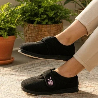 Black women’s slippers with front strap and pink floral logo on cushioned sole