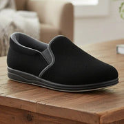Black slip-on men’s slippers with grey collar trim and flexible rubber sole.
