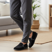 Black slip-on slippers on feet with grey pants; simple collar and cushioned sole.