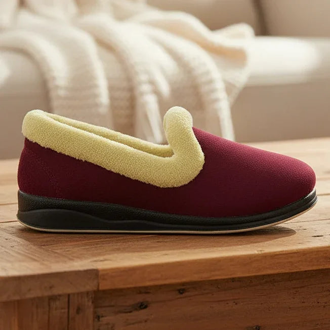 Burgundy slipper with thick beige sherpa strap and black rubber sole on wooden step
