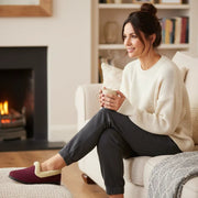 Burgundy sherpa-lined slippers on seated woman’s feet with low black sole