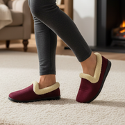 Burgundy slippers with beige sherpa trim worn by standing woman on carpet