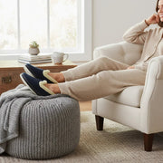 Navy plush slip-on slippers with light tan paw appliqué, worn by seated person