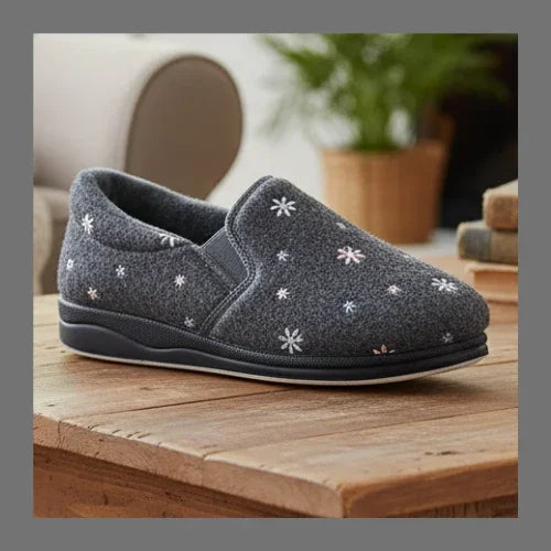 Grey slip-on slippers with white embroidered flowers and dark edging on a wooden step